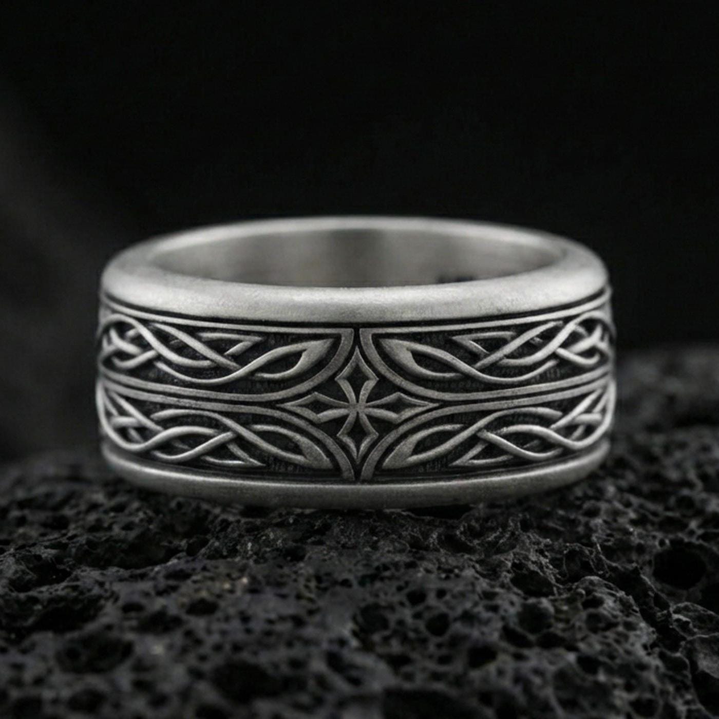 Oxidized sterling silver elven star spinner band ring on dark volcanic rock, Celtic knotwork and star motif on rotating center, premium macro product shot.