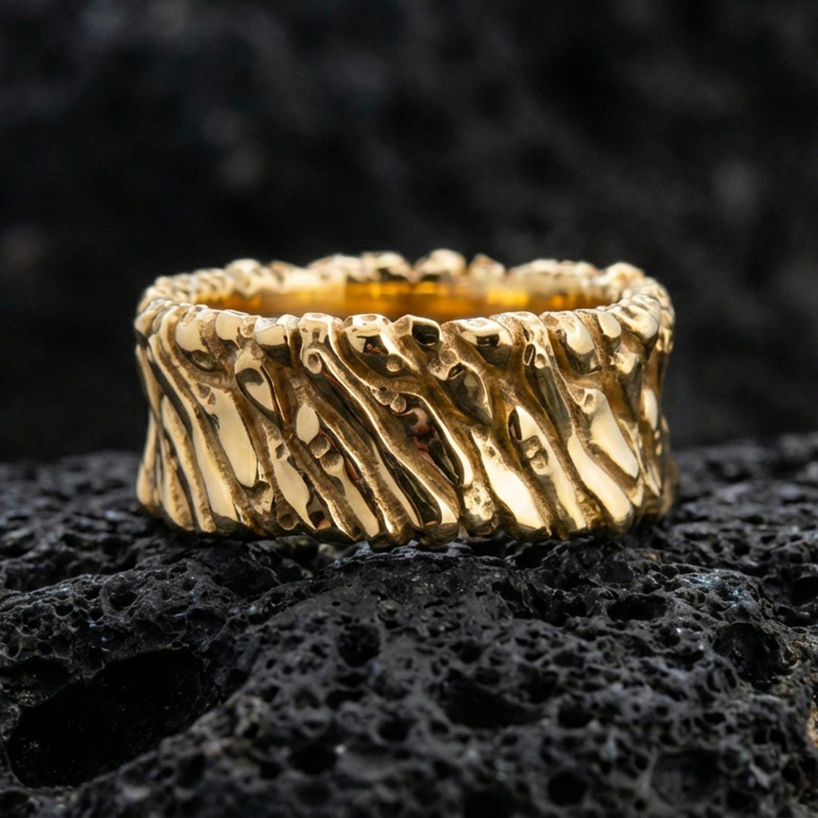 Gold plated twisted rope texture band ring on volcanic rock, detailed spiral cable pattern with bold depth, luxury jewelry product photography.