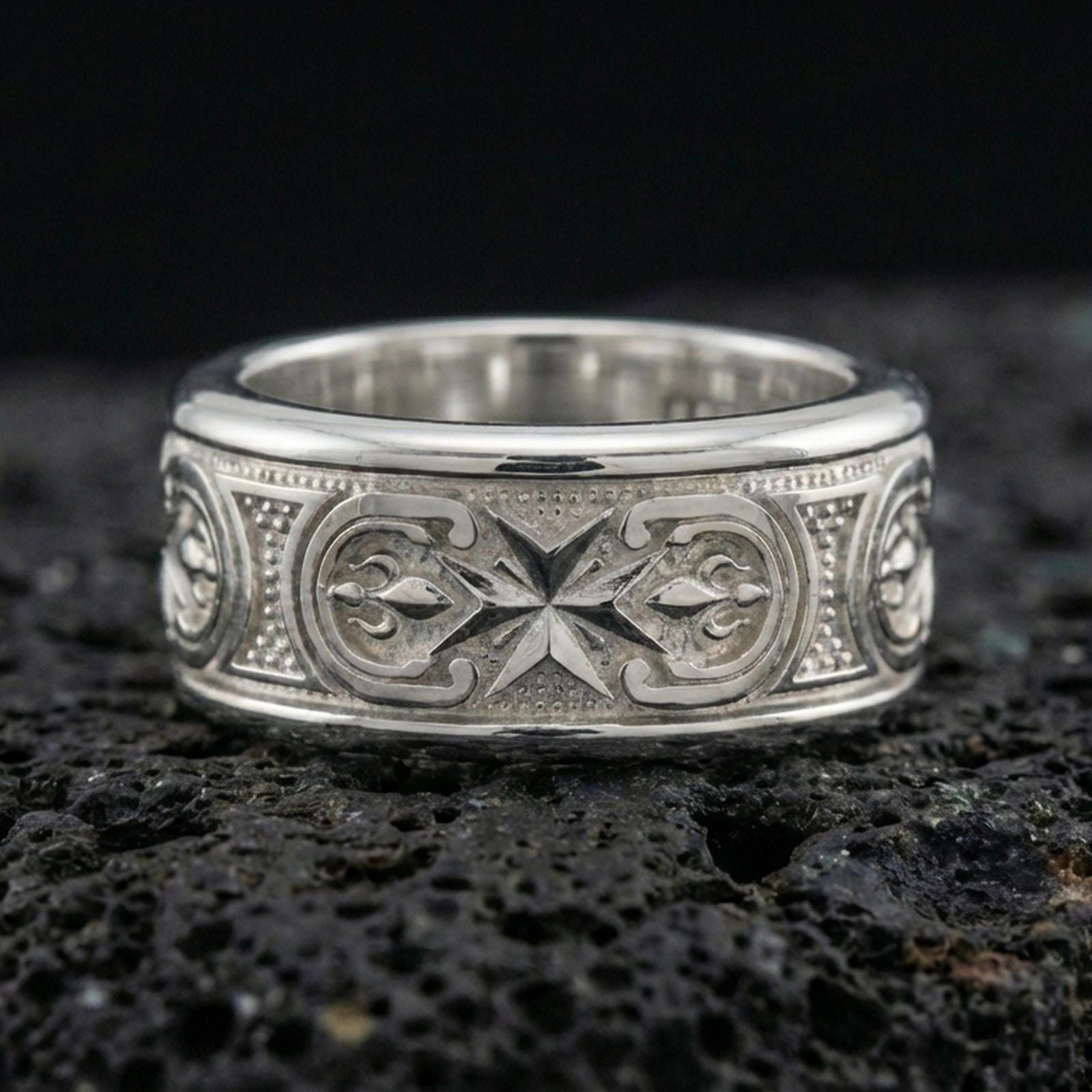 Polished silver Maltese cross fidget spinner ring on black volcanic stone, crisp cross relief with detailed scroll accents, centered close-up studio lighting.