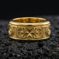 Load image into Gallery viewer, Gold plated Maltese cross spinner band ring on volcanic rock, bold cross motif on rotating band with ornamental panel detail, luxury jewelry product photography.
