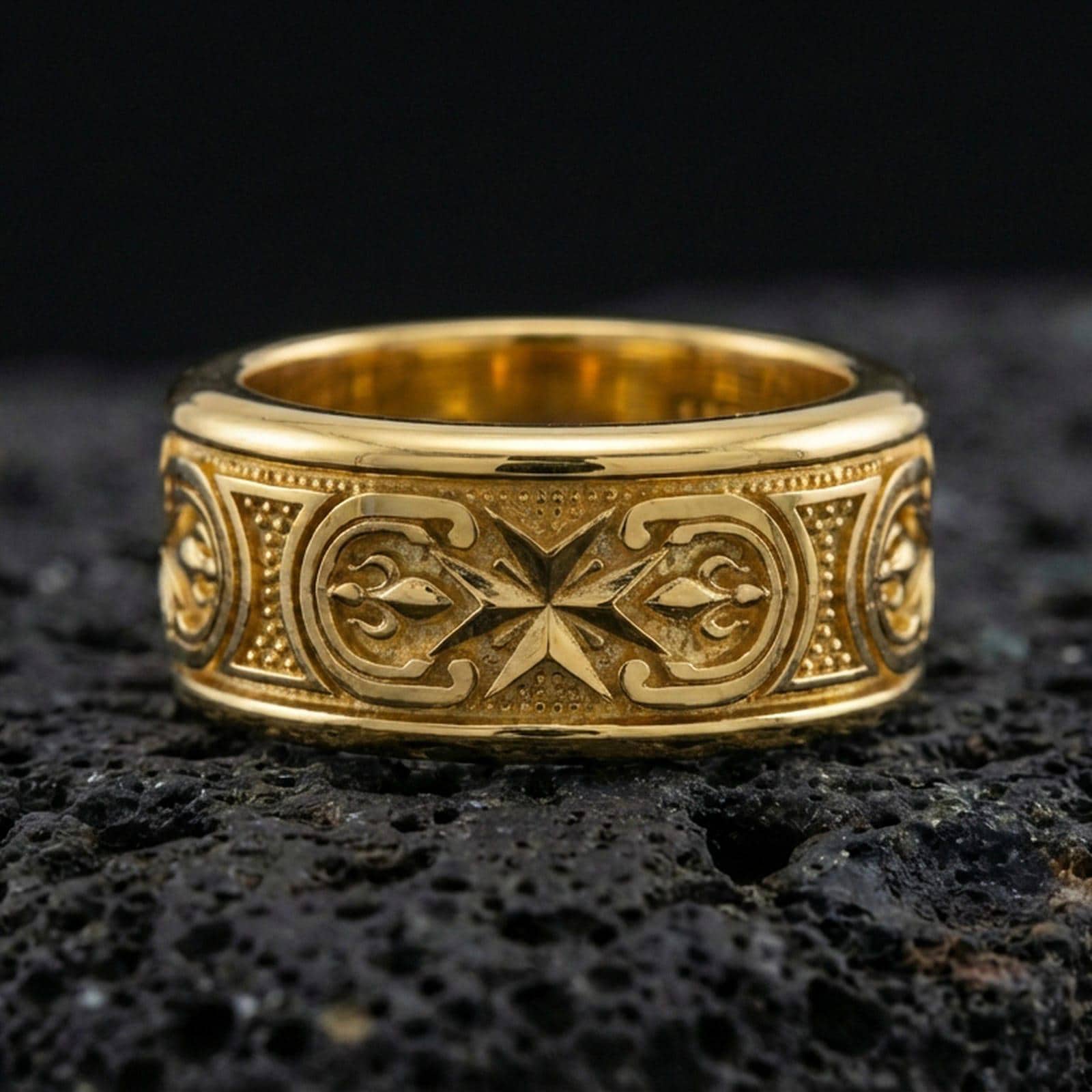 Gold plated Maltese cross spinner band ring on volcanic rock, bold cross motif on rotating band with ornamental panel detail, luxury jewelry product photography.