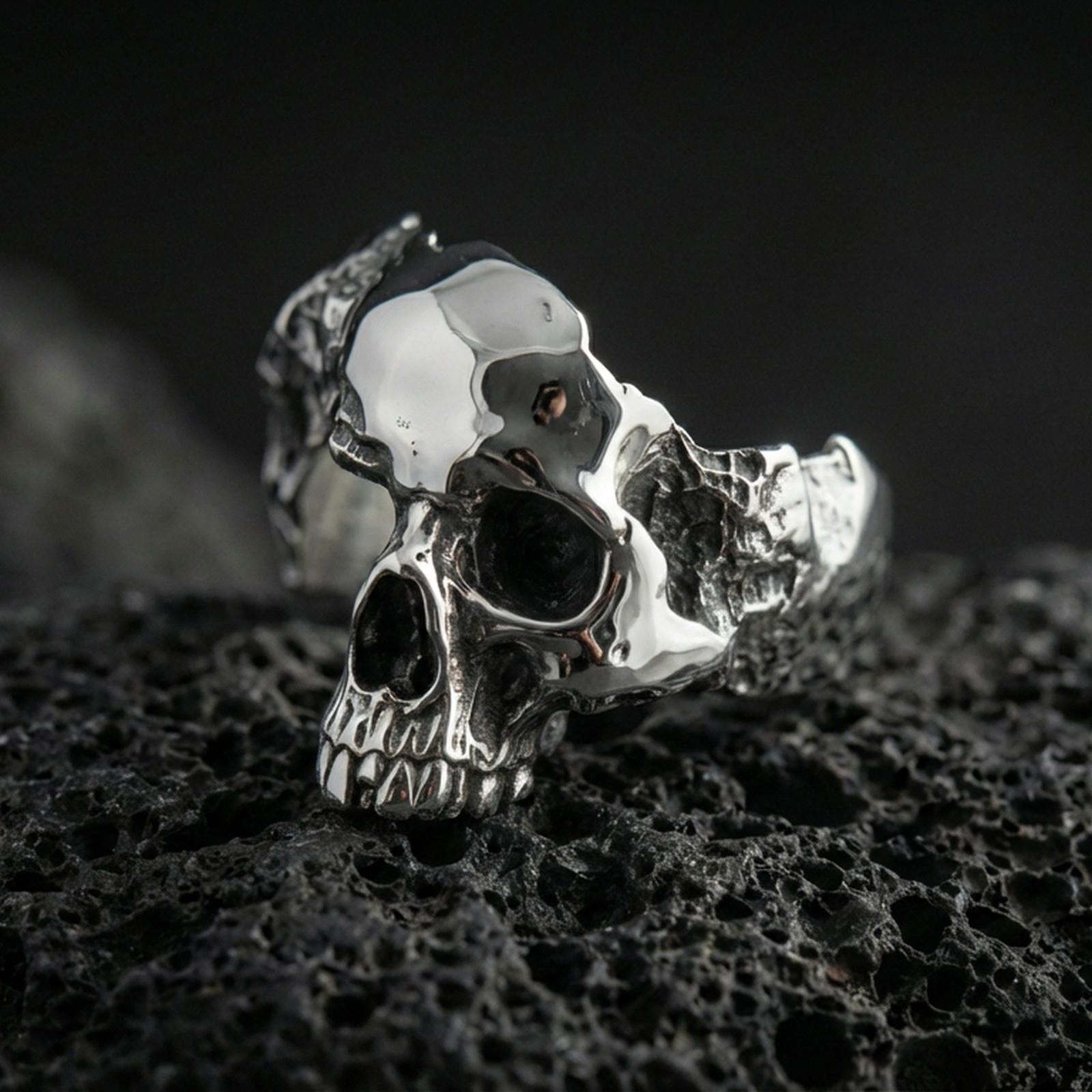 Sterling silver shattered skull ring in a polished silver finish, sculpted skull face with broken-style edges and bold unisex profile, close-up on volcanic stone