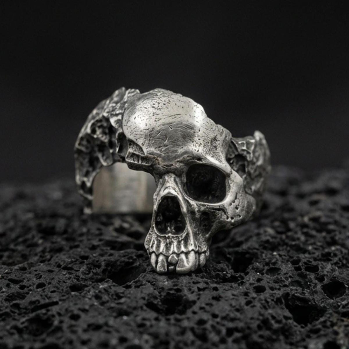 Sterling silver shattered skull ring with an oxidized finish, openwork skull design and rugged gothic texture, macro on black volcanic rock