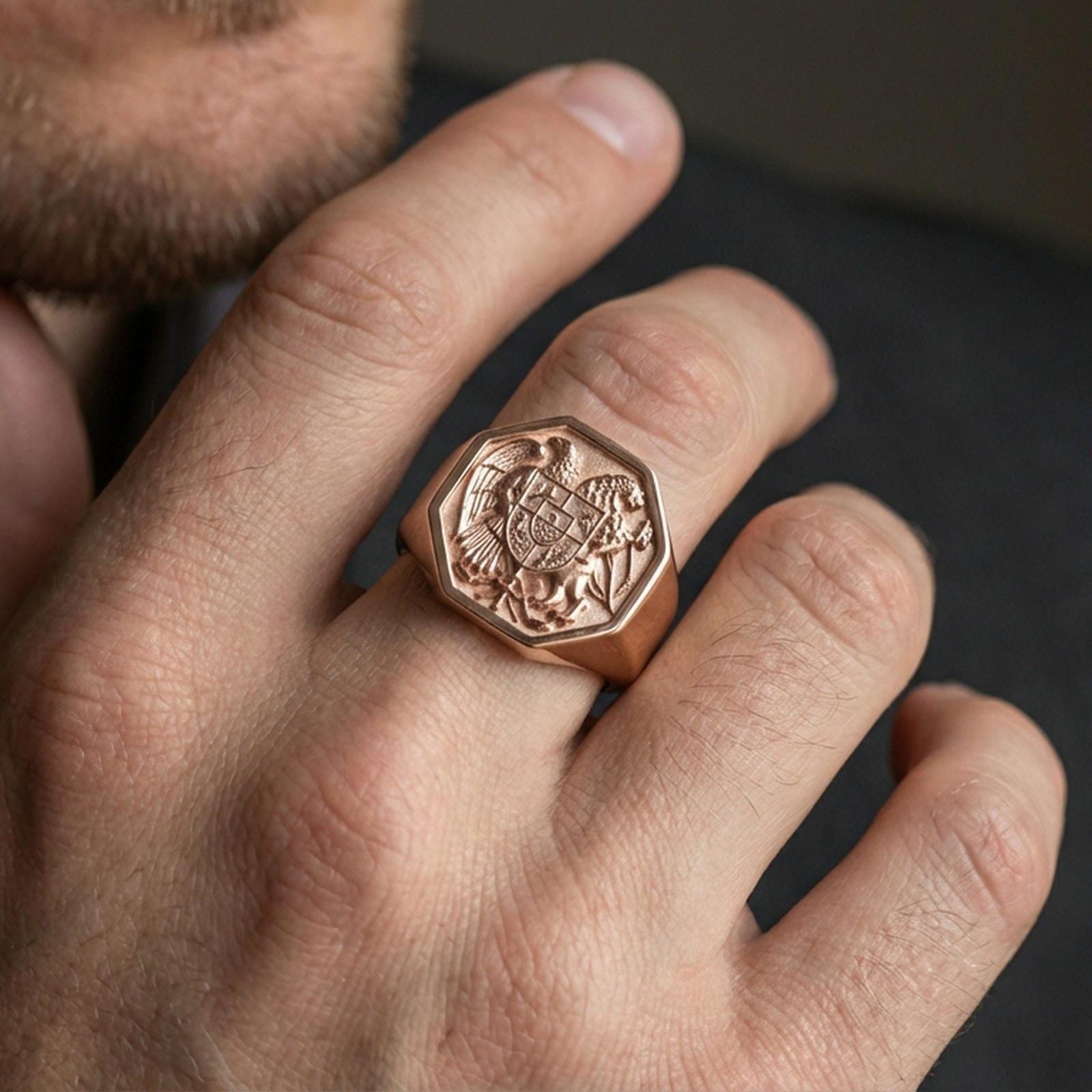 Sterling silver Armenian coat of arms signet ring on a finger, macro lifestyle shot featuring the rose gold plated finish and engraved heraldic emblem details