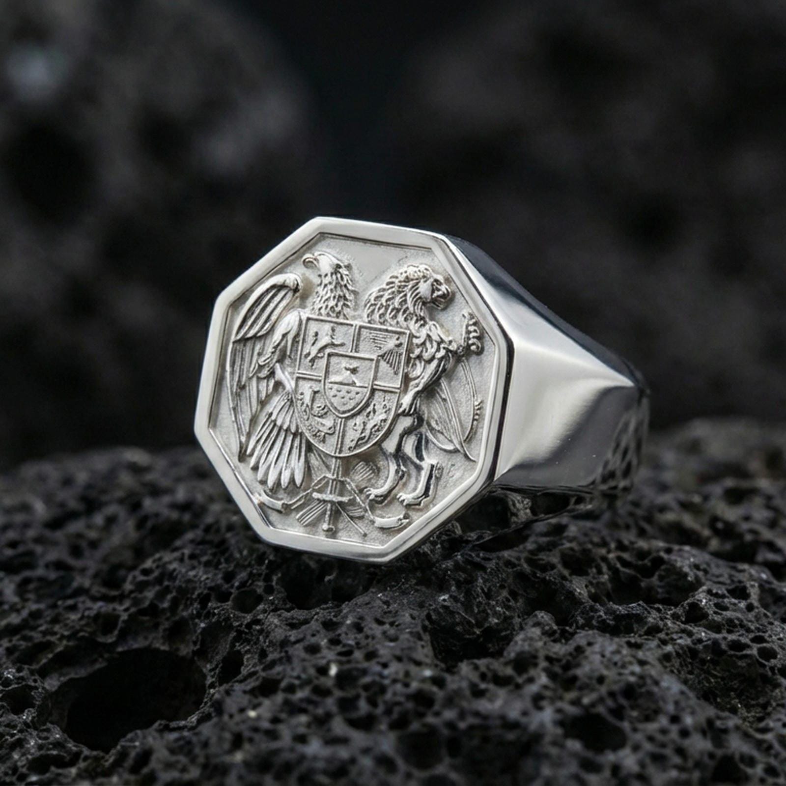 Sterling silver Armenian coat of arms signet ring in a polished silver finish, detailed heraldic emblem with shield, eagle and lion relief, close-up on volcanic stone