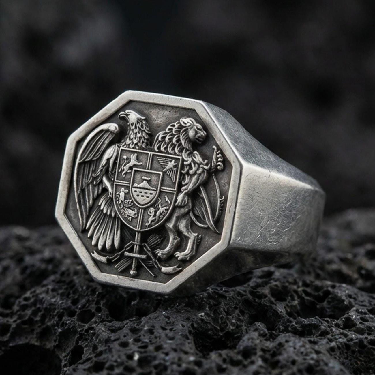 Sterling silver Armenian coat of arms signet ring with an oxidized finish, octagonal face featuring eagle and lion heraldic crest, macro on black volcanic rock