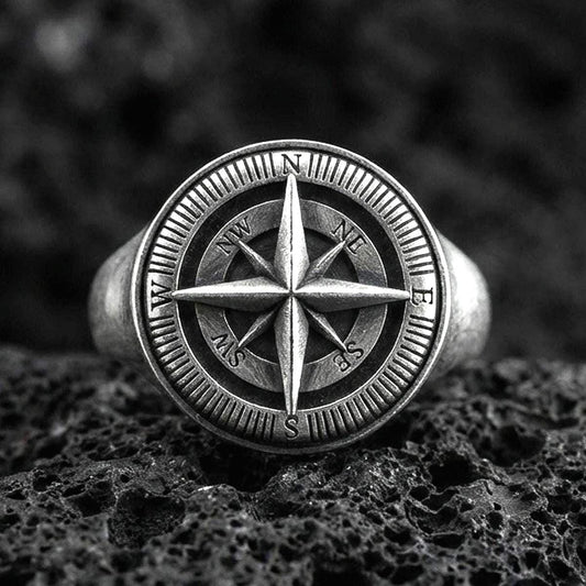 Sterling silver compass rose signet ring with an oxidized finish, engraved cardinal directions and nautical star design, macro on black volcanic rock