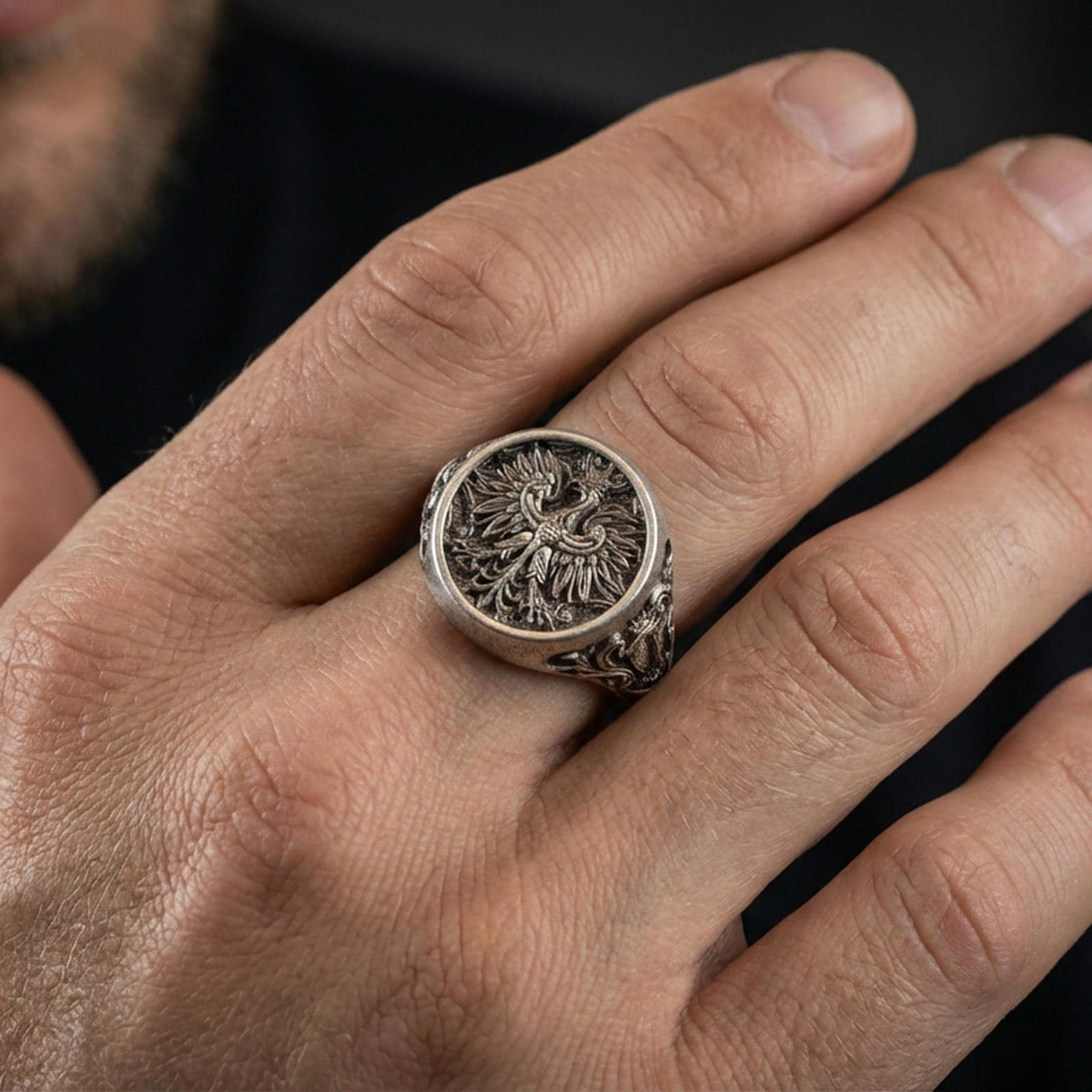 Sterling silver phoenix signet ring worn on a finger, close-up lifestyle shot highlighting the oxidized engraved crest and detailed feather motif