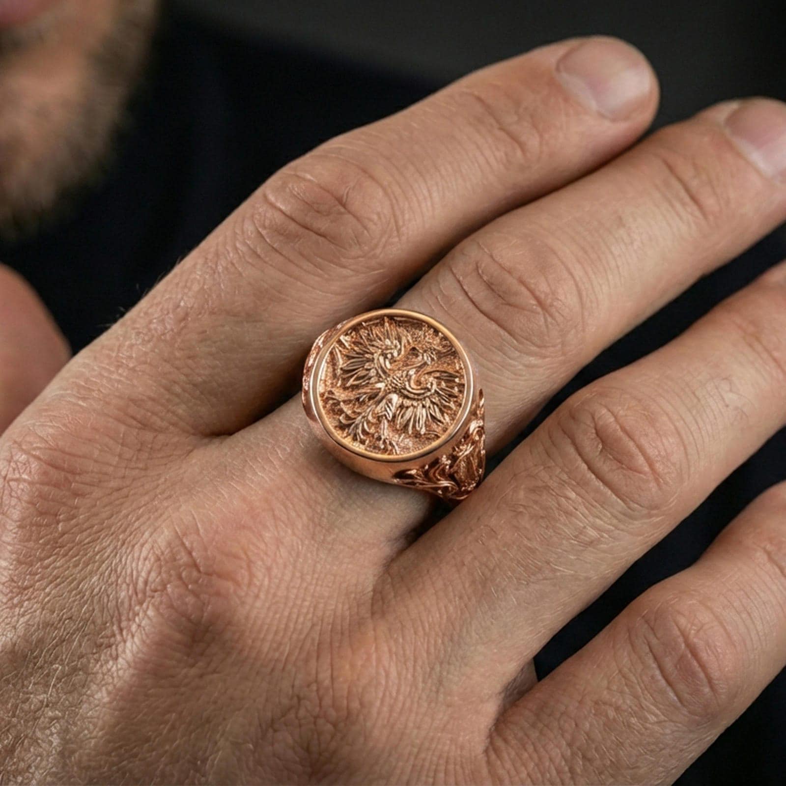 Sterling silver heraldic phoenix ring on a finger, macro lifestyle shot featuring the rose gold plated finish and intricate engraved emblem details