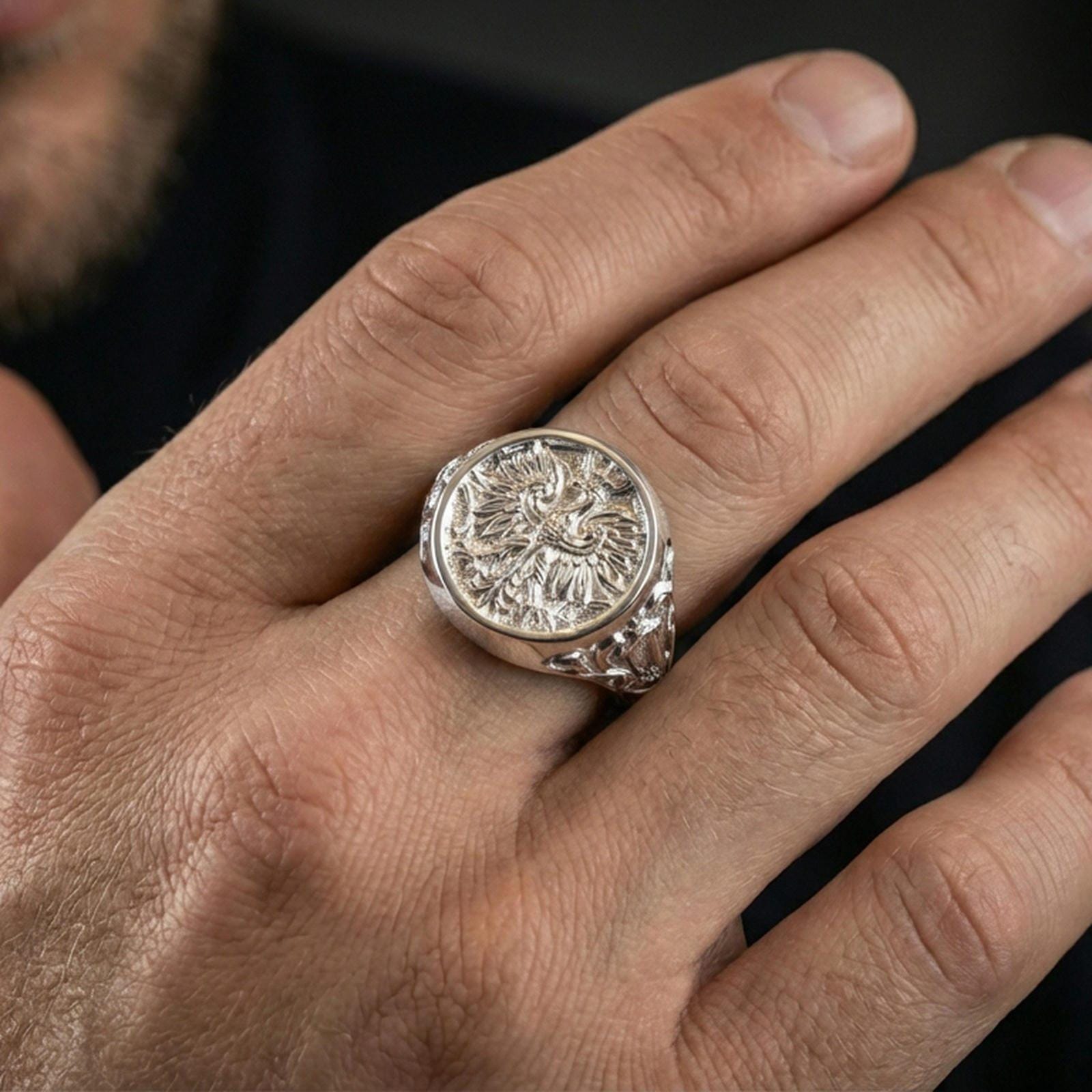 Sterling silver mythical bird signet ring on a finger, macro lifestyle image emphasizing the polished silver finish and ornate phoenix face engraving