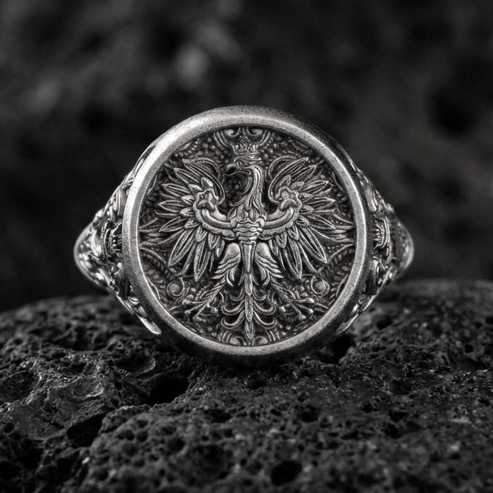 Sterling silver phoenix signet ring with an oxidized finish, round face engraved with a detailed heraldic phoenix motif, macro on black volcanic rock