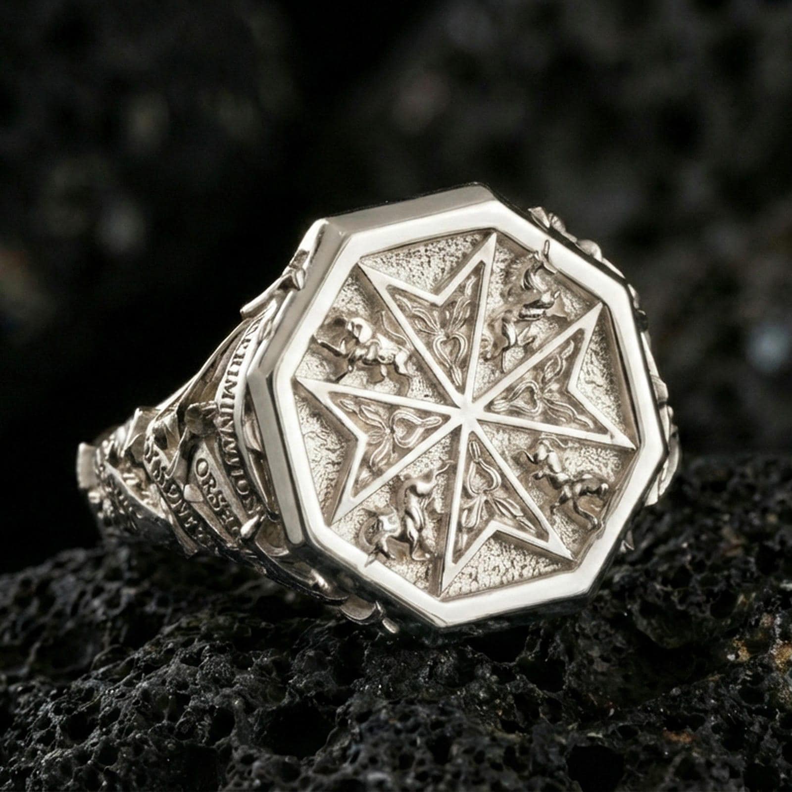 Sterling silver Maltese cross statement ring in a polished silver finish, bold octagonal signet design with engraved cross motif and textured background, close-up on volcanic stone
