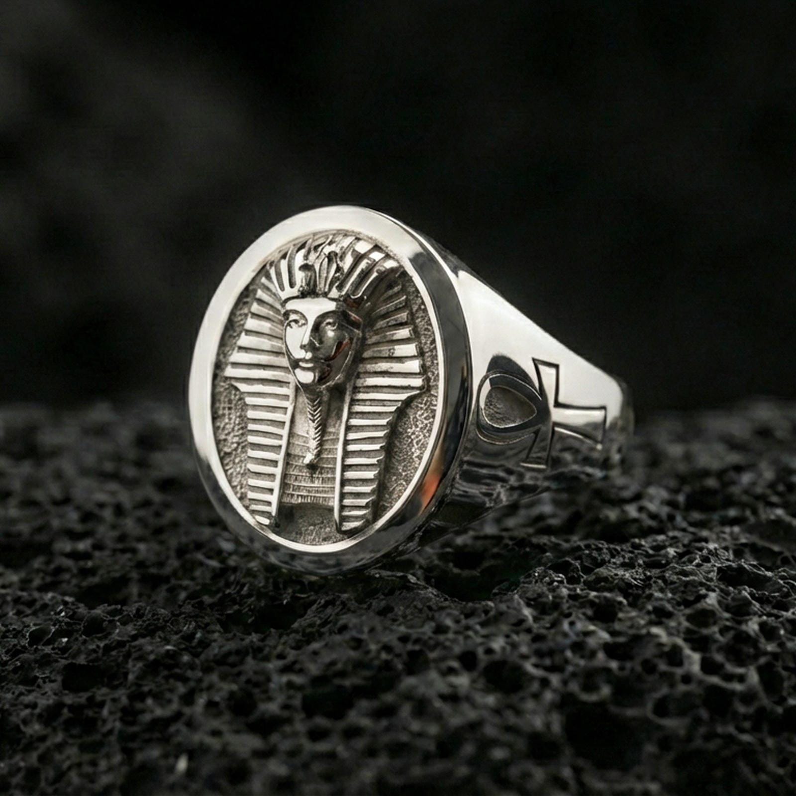 Sterling silver pharaoh ring in a polished silver finish, oval signet design with detailed Egyptian headpiece relief and engraved ankh shoulder accent, close-up on volcanic stone