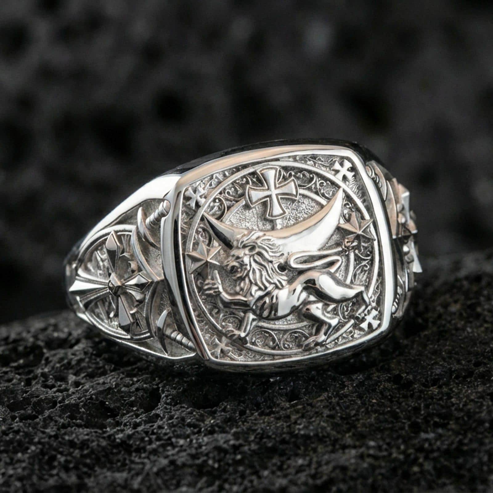 Sterling silver heraldic lion ring in a polished silver finish, bold signet design with raised lion emblem, cross motif, and engraved side symbols, close-up on volcanic stone