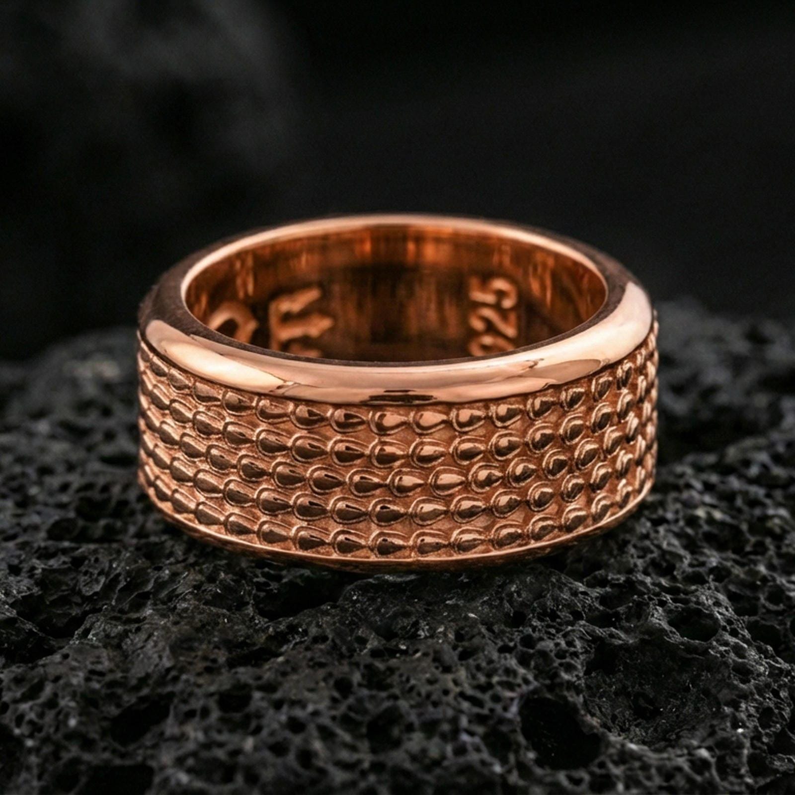 Rose gold plated sterling silver scale band on volcanic stone, sculpted teardrop scale texture with strong contrast, minimal high-end close-up.