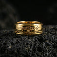 Load image into Gallery viewer, Gold plated Yggdrasil spinner band ring on volcanic rock, detailed tree of life engraving on rotating band, luxury jewelry product photography.
