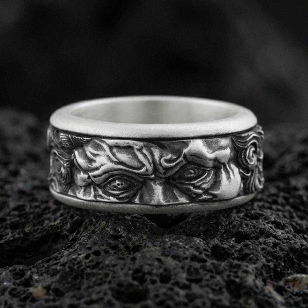 Oxidized sterling silver Michelangelo Moses spinner band ring on dark volcanic rock, Renaissance-inspired face relief on rotating center, premium macro product shot.