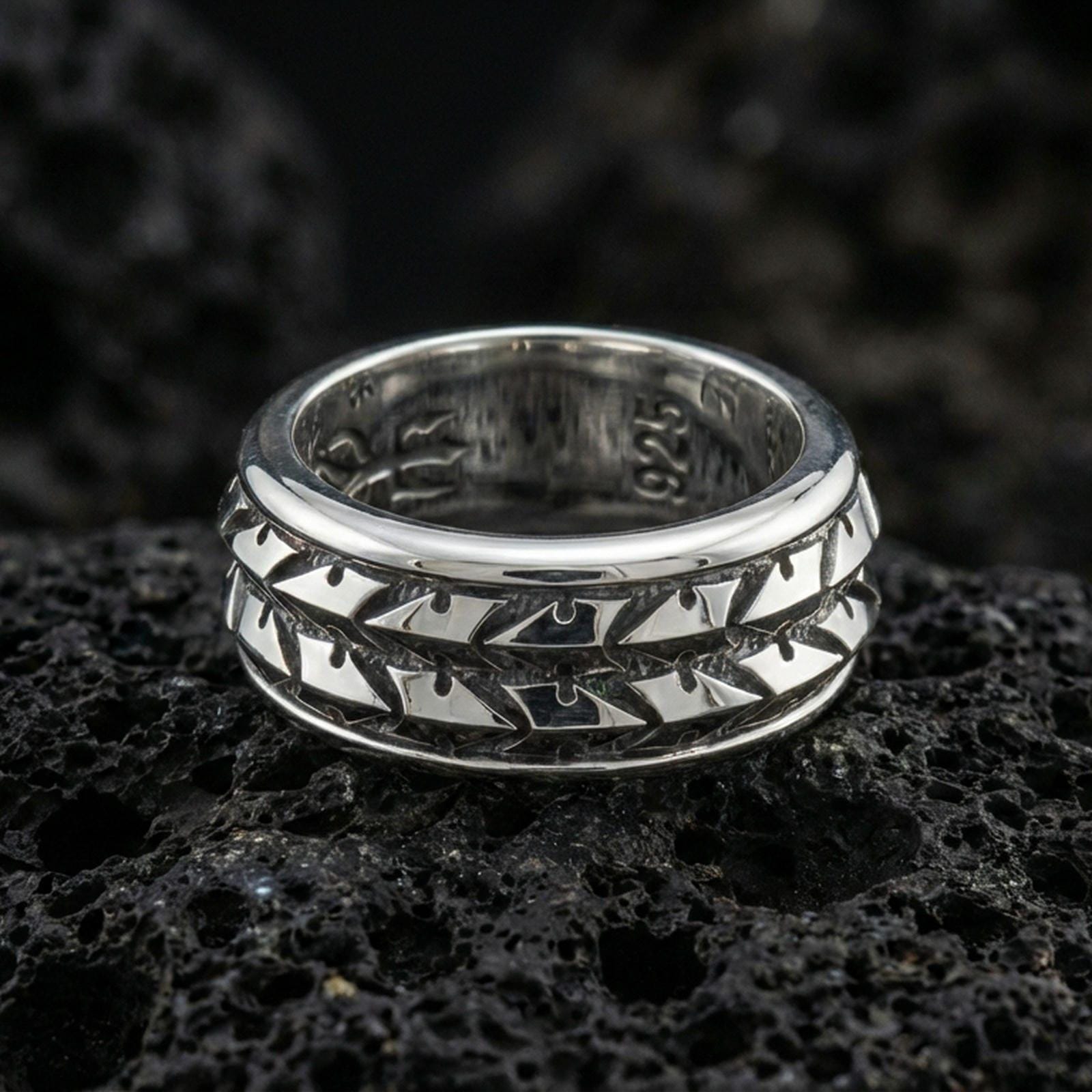 Polished silver arrowhead fidget spinner ring on black volcanic stone, crisp repeating arrow motif with smooth comfort edges, centered close-up studio lighting.