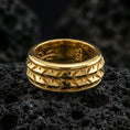 Load image into Gallery viewer, Gold plated arrowhead spinner band ring on volcanic rock, detailed tribal arrow pattern on rotating band, luxury jewelry product photography.
