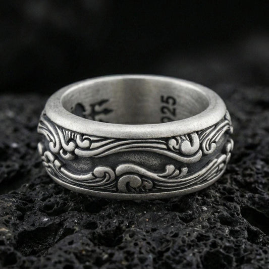 Oxidized sterling silver scrollwave spinner band ring on dark volcanic rock, flowing wave filigree engraving on rotating center, premium macro product shot.