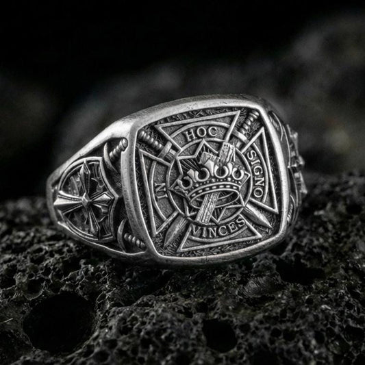 Sterling silver Templar shield ring with an oxidized finish, engraved crusader cross, crown and sword emblem with Latin inscription, macro on black volcanic rock