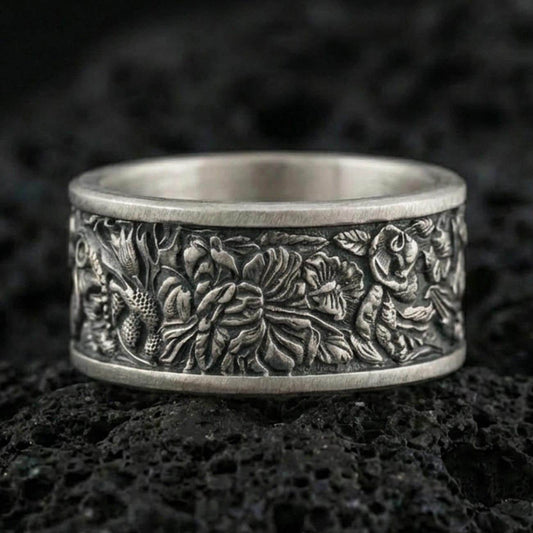 Oxidized sterling silver jungle wildlife band ring on dark volcanic rock, high-relief leaves and exotic animal engraving, premium macro product shot.