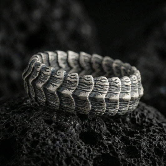 Oxidized sterling silver dragon scale band ring on dark volcanic rock, rugged segmented ridge texture with deep contrast, premium macro product shot.