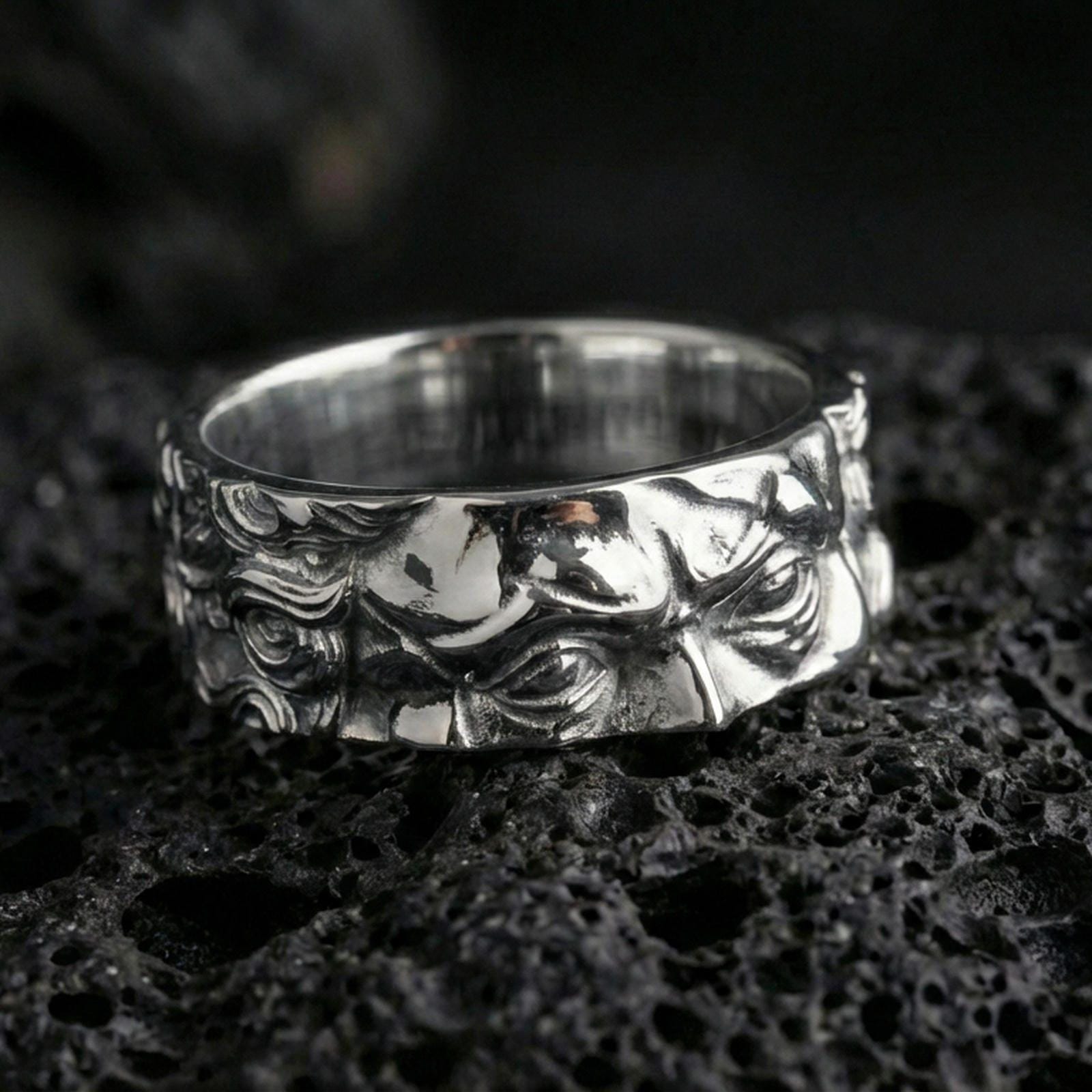 Polished silver Moses fidget spinner ring on black volcanic stone, crisp sculpted face relief with ornamental scroll side detail, centered close-up studio lighting.