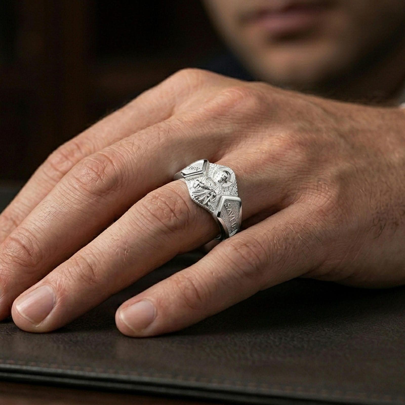 Polished silver Saint Jude religious signet ring on finger, crisp icon relief with engraved text panels, refined everyday wear close-up.
