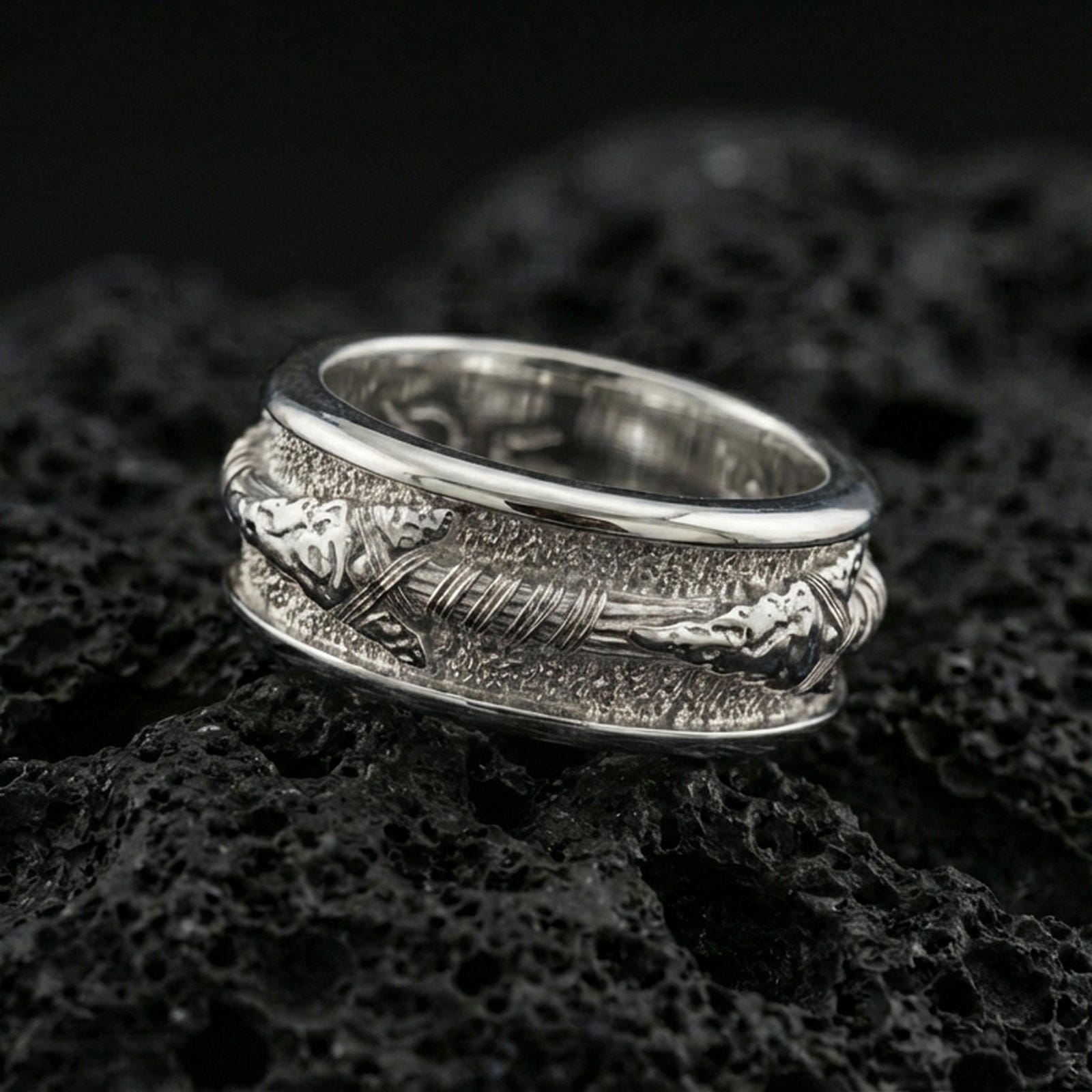 Polished silver arrow fidget spinner ring on black volcanic stone, crisp arrowhead and wire-wrapped shaft detail with rugged texture, centered close-up studio lighting.