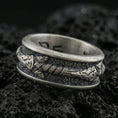 Load image into Gallery viewer, Oxidized sterling silver arrow spinner band ring on dark volcanic rock, tribal arrow and wrapped shaft detail on rotating center, premium macro product shot.
