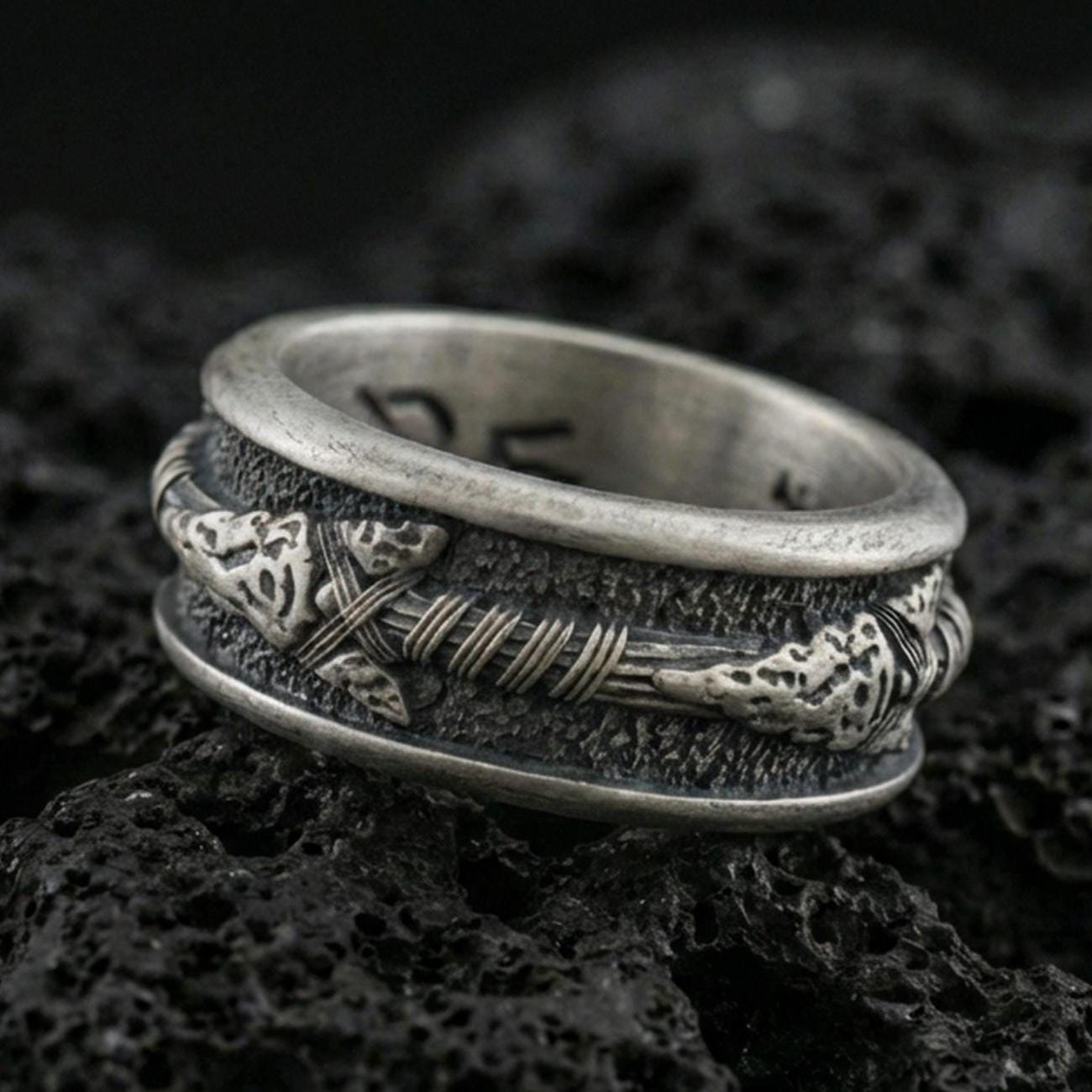 Oxidized sterling silver arrow spinner band ring on dark volcanic rock, tribal arrow and wrapped shaft detail on rotating center, premium macro product shot.