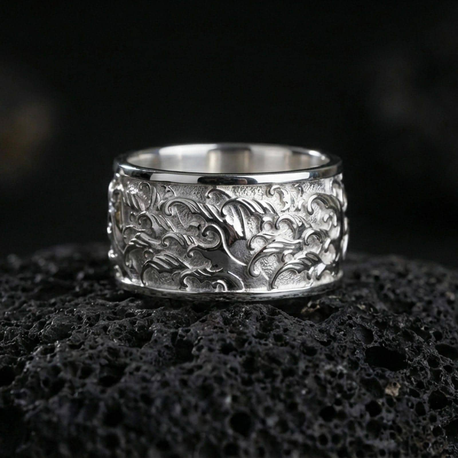 Polished silver flame swirl engraved band ring on black volcanic stone, crisp flowing fire relief with smooth comfort edges, centered close-up studio lighting.