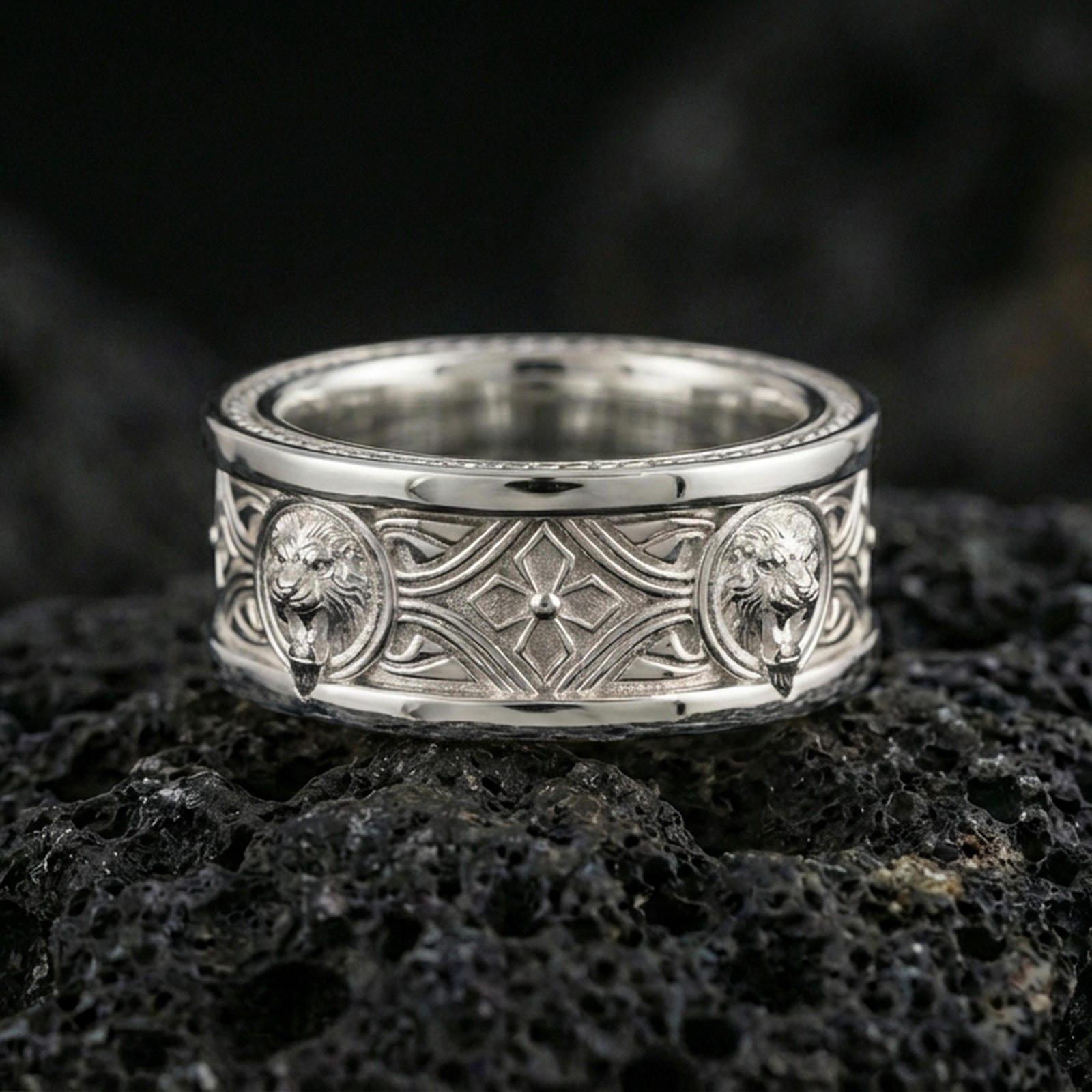 Polished silver lion crest band ring on black volcanic stone, crisp lion head relief medallions with geometric cross motif and ornate lines, centered close-up studio lighting.