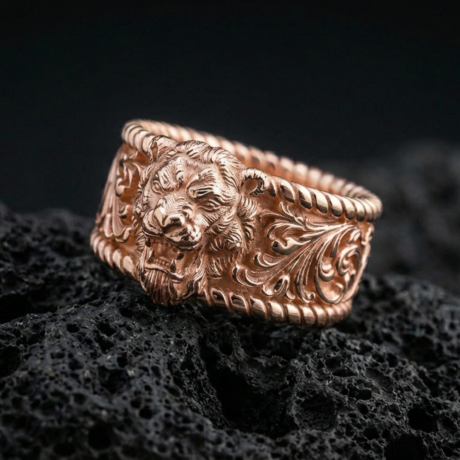 Rose gold plated sterling silver lion signet ring on volcanic stone, sculpted lion head relief with ornate scrollwork and deep contrast, minimal high-end close-up.