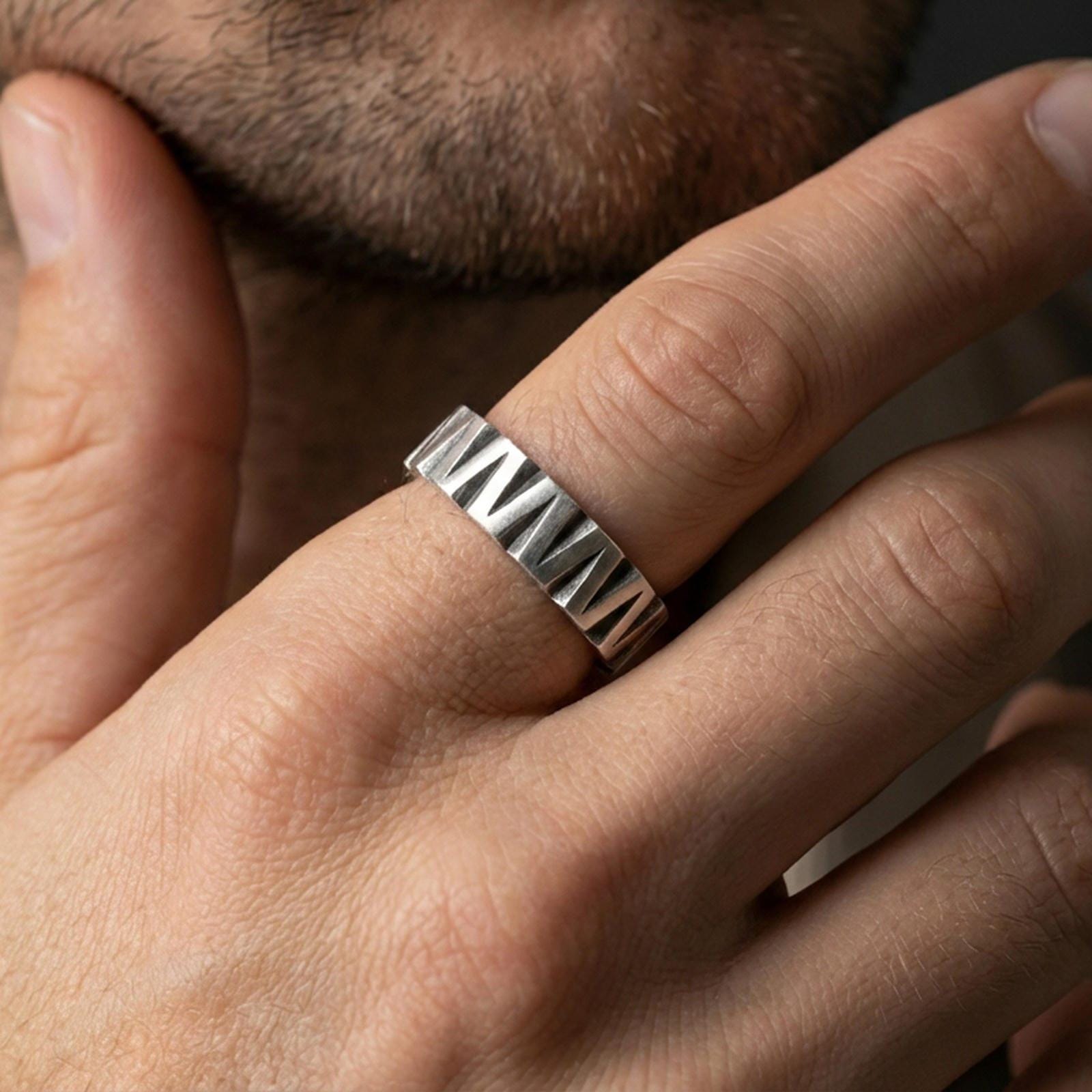 Oxidized sterling silver faceted band worn on finger, bold chevron-cut texture with dark recessed grooves, lifestyle hand close-up.