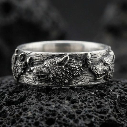Oxidized sterling silver wolf and deer band ring on black volcanic rock, high-relief animal heads with deep shadowed texture, sharp macro product photo.