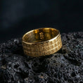 Load image into Gallery viewer, Gold plated square-grid textured ring on black volcanic stone, warm shine defining each framed square detail, high-contrast studio macro.
