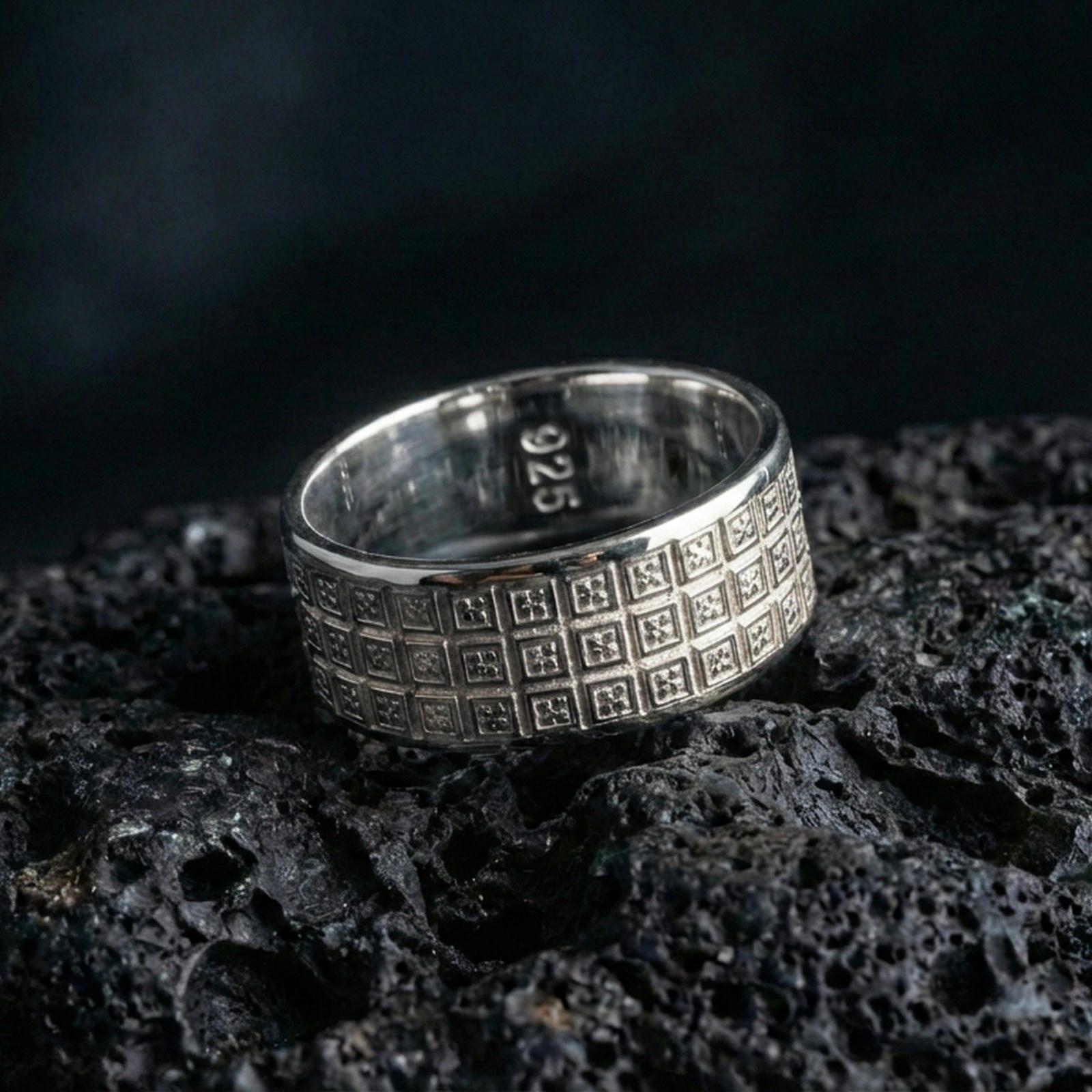 Polished silver square-grid pattern band on volcanic rock, crisp reflections on the raised borders highlighting the geometric relief, premium close-up.