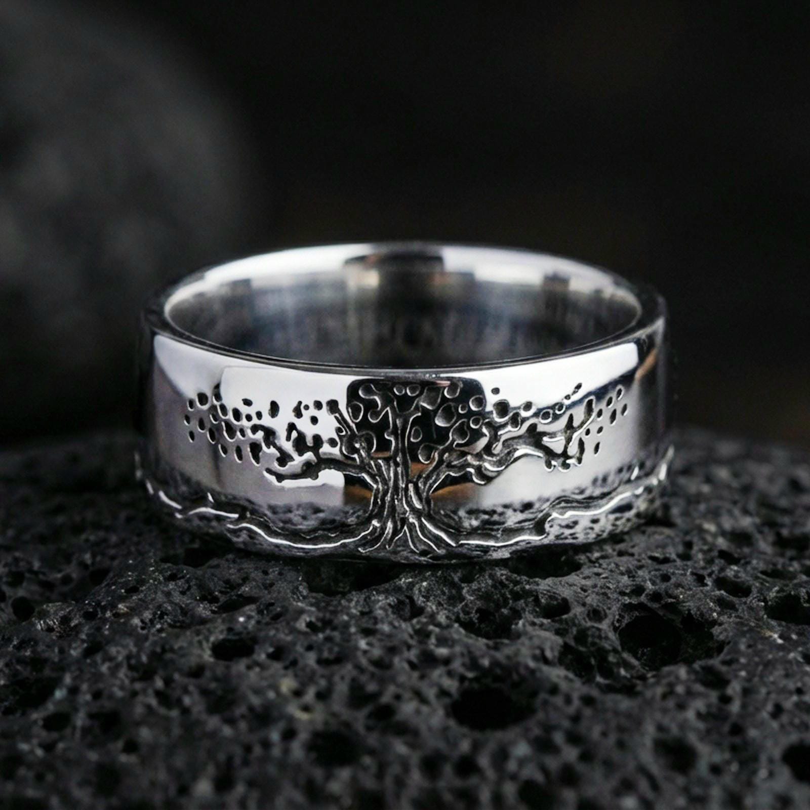 Polished silver Tree of Life engraved ring on volcanic rock, clean reflective finish highlighting the detailed canopy and root linework, premium close-up.