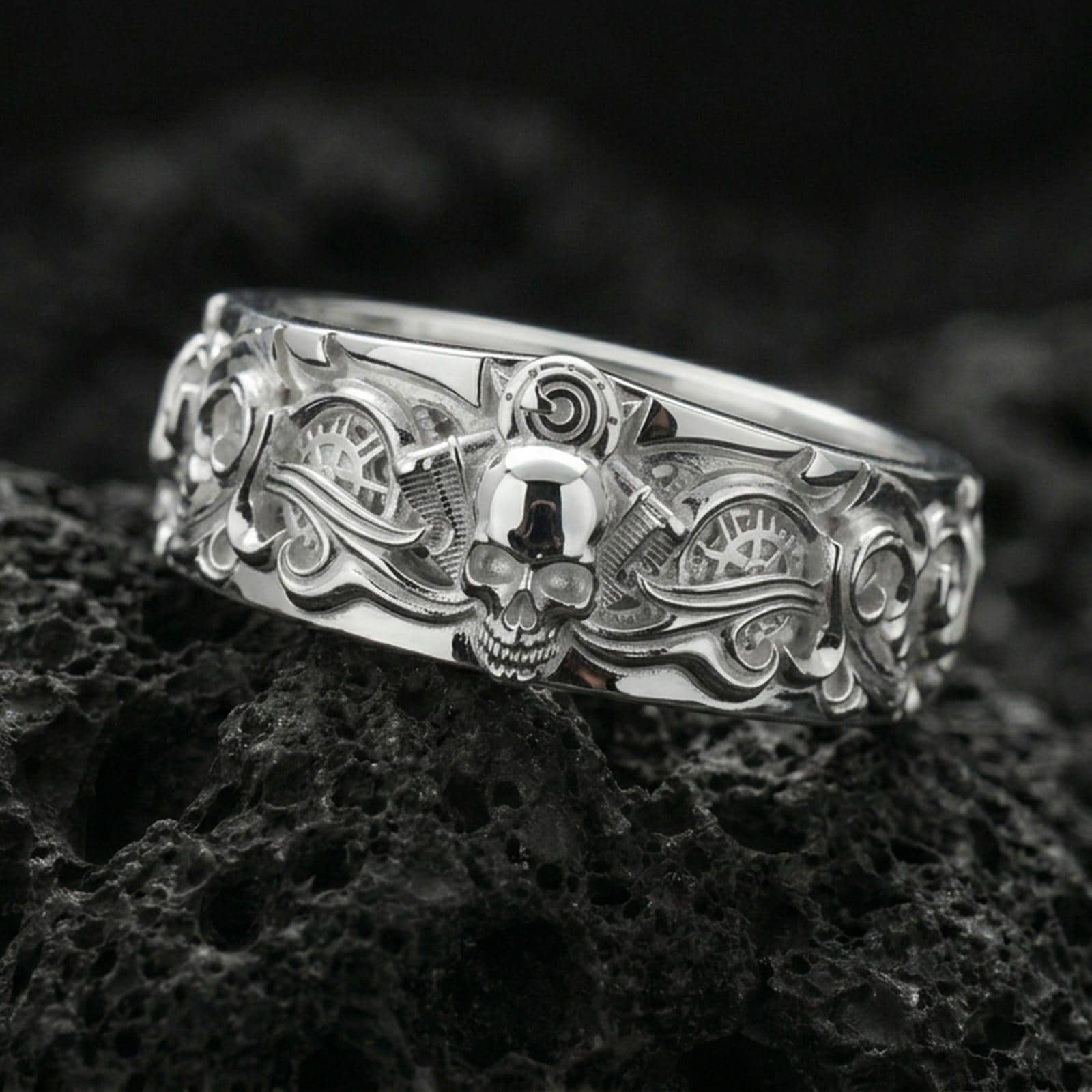 Polished silver gothic skull mechanical band ring on volcanic rock, bright reflective finish emphasizing the raised skull, flowing filigree lines, and crisp gear texture, premium close-up.
