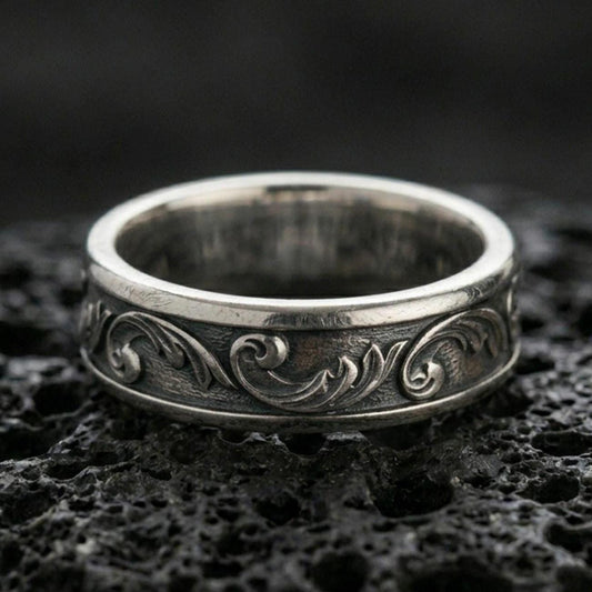 Oxidized sterling silver floral scroll band ring on black volcanic stone, vintage darkened grooves emphasizing the minimalist engraved vine pattern.
