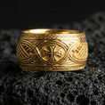 Load image into Gallery viewer, Gold plated Celtic knot and iron cross ring on black volcanic stone, warm reflective finish emphasizing the braided borders and central cross.
