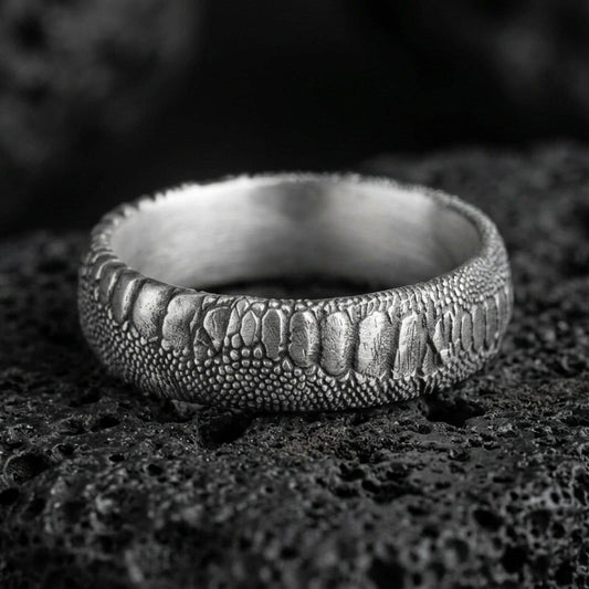 Oxidized sterling silver serpent skin band ring on black volcanic stone, scaled texture with deep shadowed recesses for a rugged gothic look.