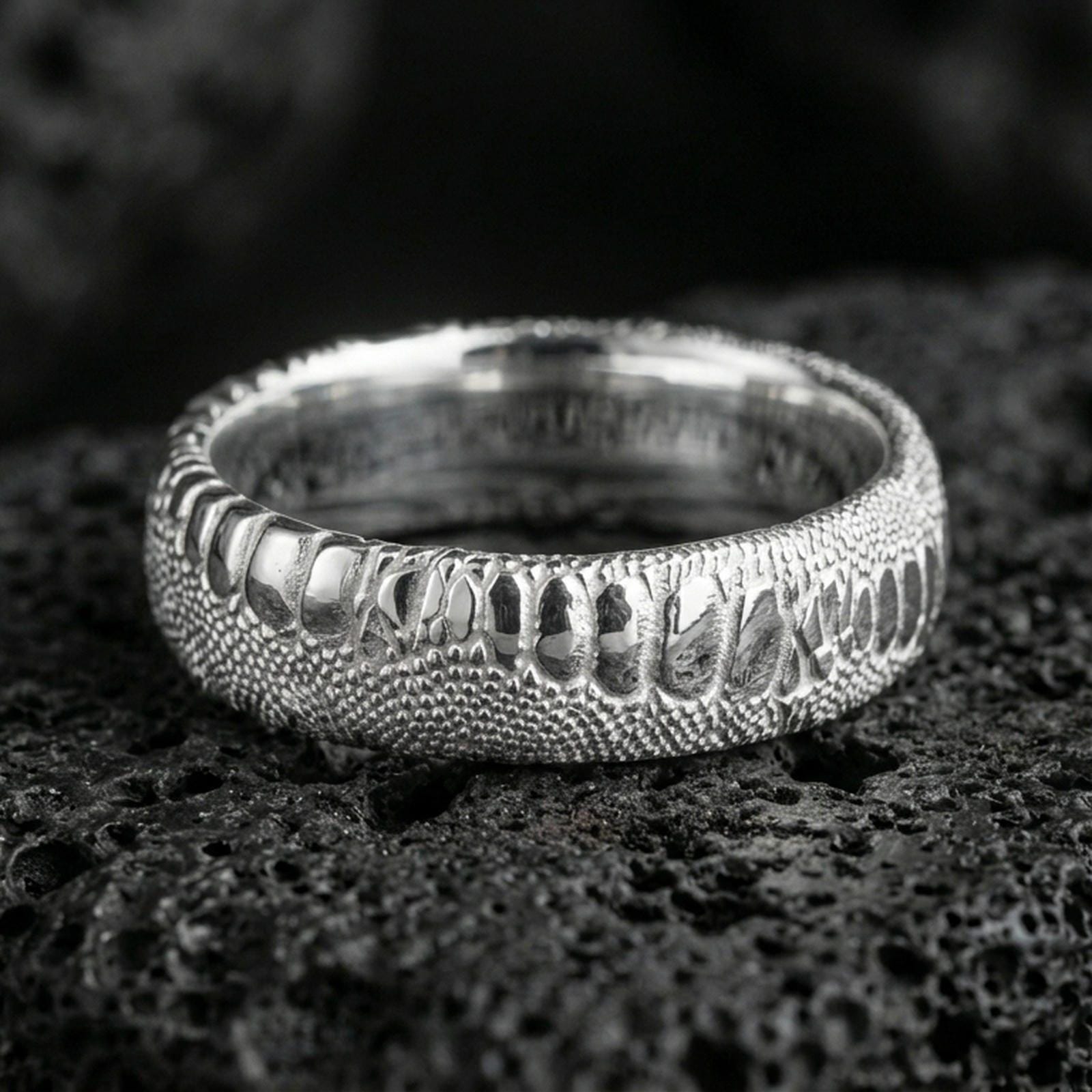 Polished silver snake scale wedding band on volcanic rock, crisp reptile pattern and smooth comfort fit captured in sharp macro detail.