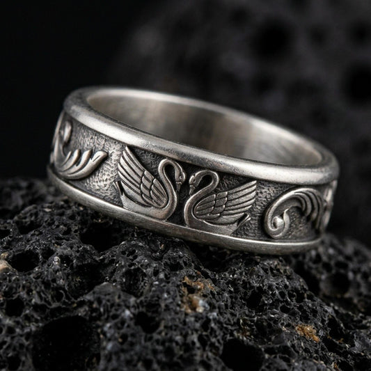 Sterling silver swan band ring photographed on volcanic rock with oxidized contrast bringing out the carved wings and textured background.