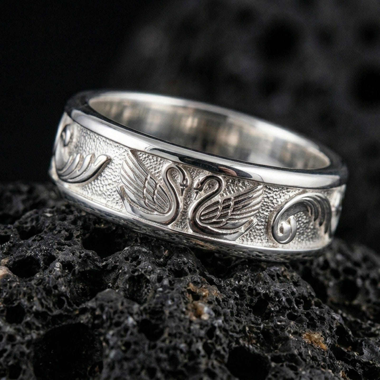 925 silver swan motif ring on black volcanic stone, polished silver edges framing the detailed engraved swans.