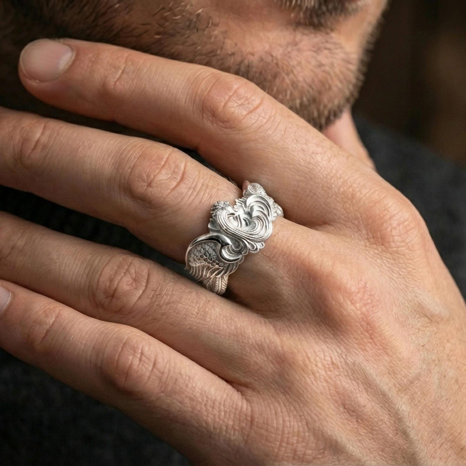 Polished silver rooster ring on a finger, clean reflective edges with high-relief feather carving across the sides.