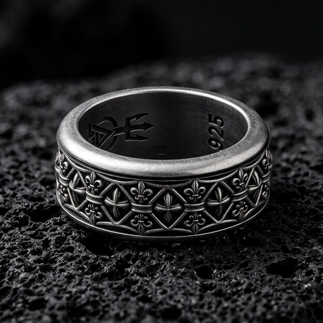 Sterling silver fleur de lis band ring photographed on volcanic rock with oxidized contrast revealing the repeating medieval pattern.