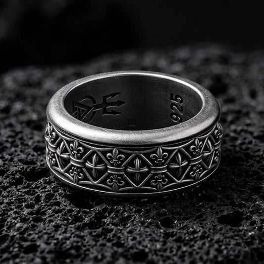 Sterling silver fleur de lis band ring photographed on volcanic rock with oxidized contrast revealing the repeating medieval pattern.